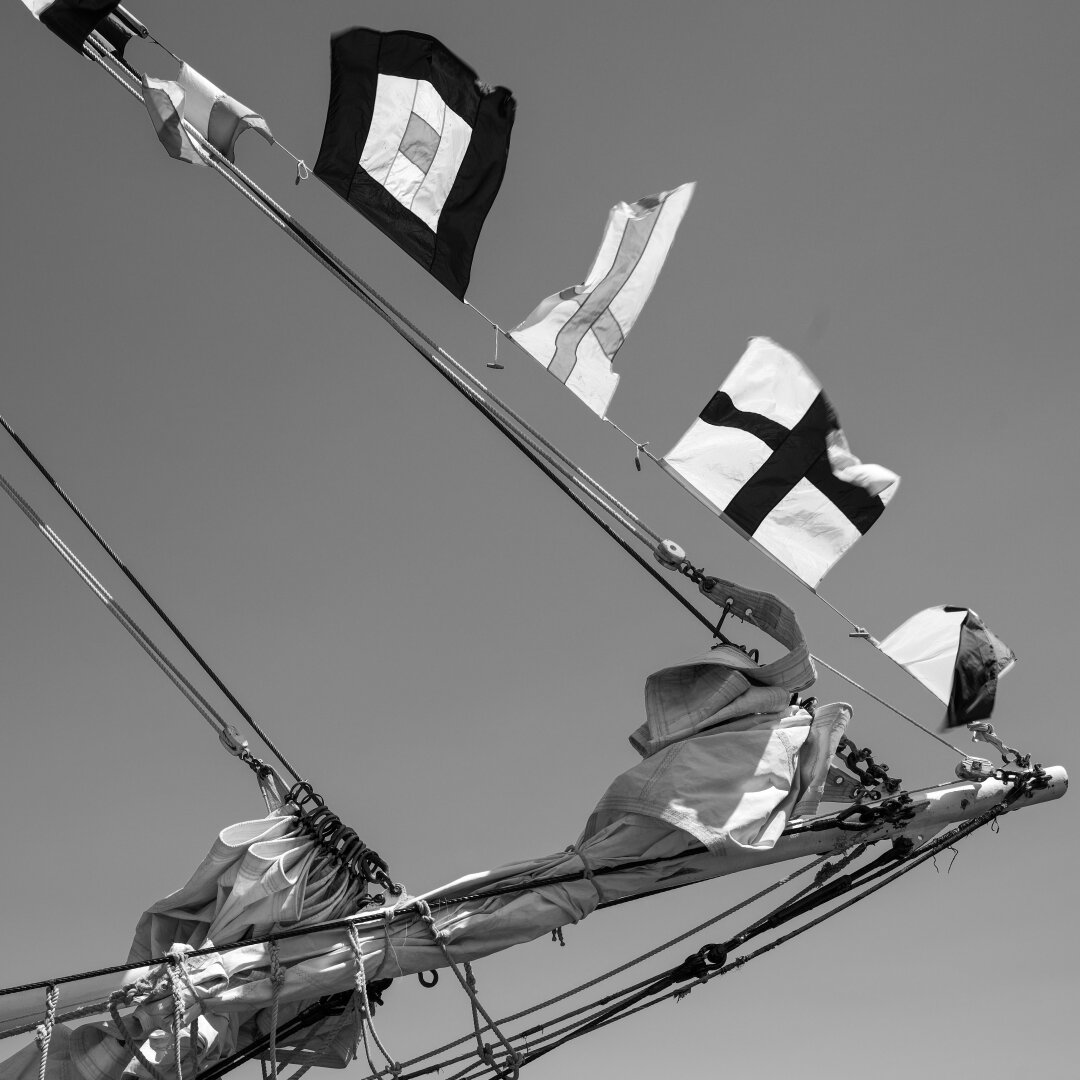 Nautical flags on a line from the bow of a sailing ship, heading up towards the mast.