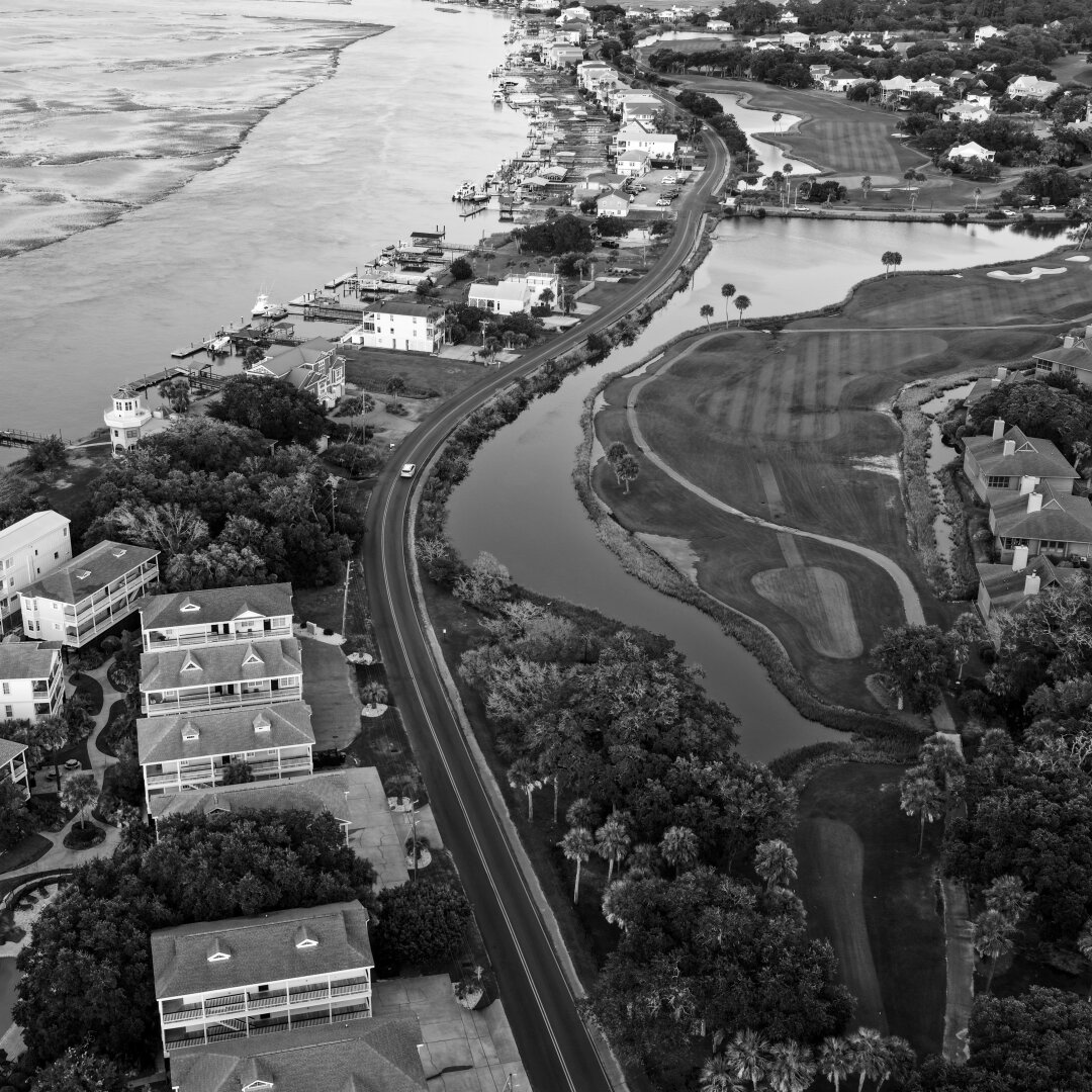Aerial shot of a street forming an S turn between a golf course and a marshy ocean terrain.